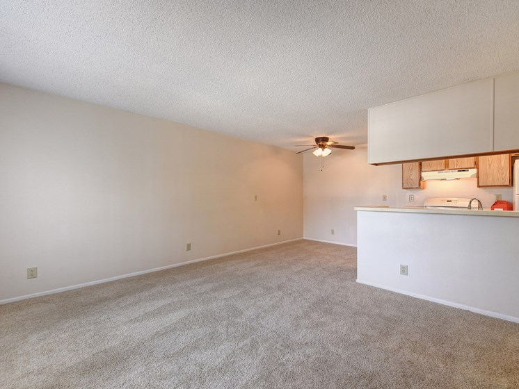 Vacant apartment living Room with views of the kitchen area.  Ceiling fan near the kitchen area